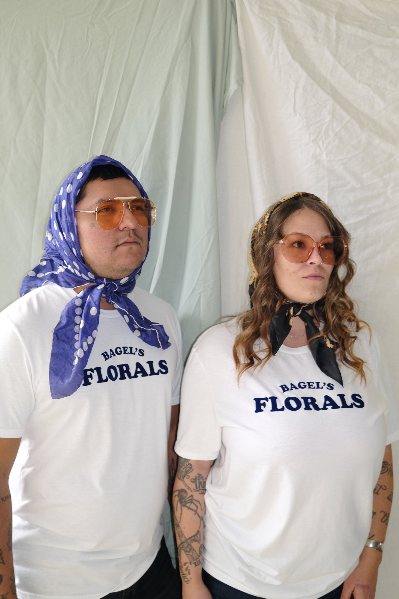 Two people wearing bandanas and white tees that read "Bagel&
