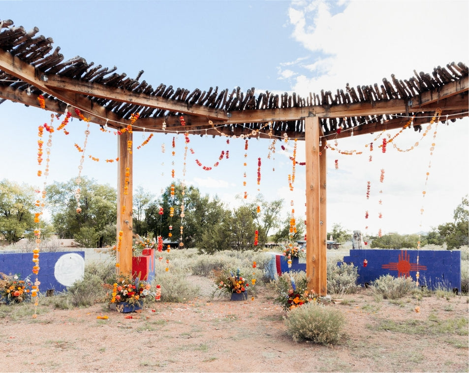 Orange and red handmade garland hung over wooden structure for a wedding by Bagel's Florals in ABQ