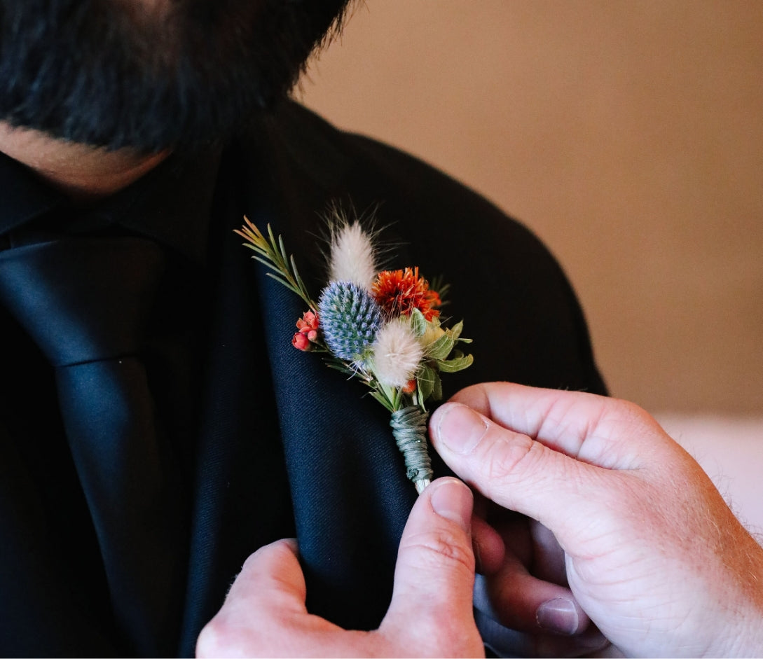 Hand adjusting a grooms dark floral lapel created by ABQ Flower Designer, Bagel's Florals