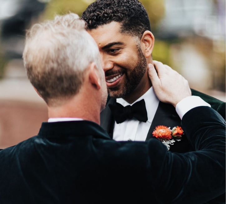 a close up portrait of two grooms embracing with the focus on an orange floral lapel by Bagel's Florals in New Mexico